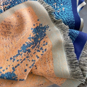 Detailed view of thick jacquard scarf with orange and navy color blocking and fringe edge