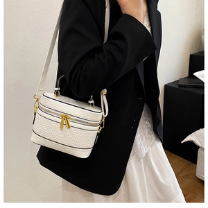 Close-up of white textured leather box bag with gold hardware and leather strap