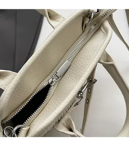 Detail of smooth silver zipper closure and lychee grain leather on cream tote bag