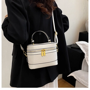 Detail of white textured box bag with gold zippers and black piping on black coat