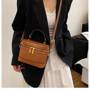 Detail of a brown box-shaped crossbody bag featuring textured PU leather and gold zippers