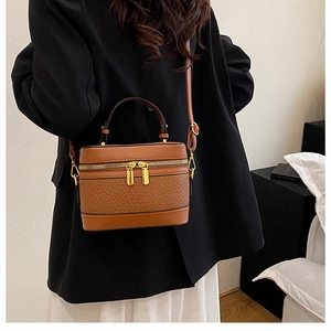 Detailed view of brown textured leather box bag with dual gold zippers and metal hardware