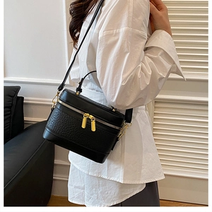 Detail of a black textured box bag featuring gold double zippers and a sleek top handle