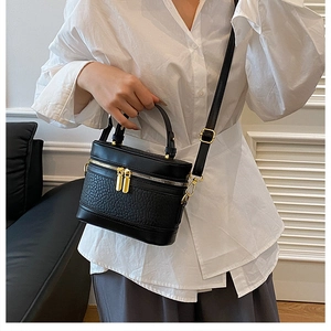Detail of black textured leather bucket bag with gold zippers and adjustable shoulder strap