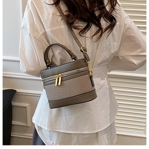 Detail of grey textured crossbody box bag with gold zippers shown on a model