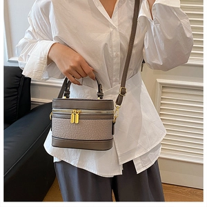 Detail of grey-brown leather barrel bag featuring gold zippers and textured lychee grain