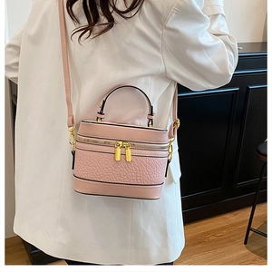 Close-up of pink textured leather crossbody box bag with gold zippers and white blazer