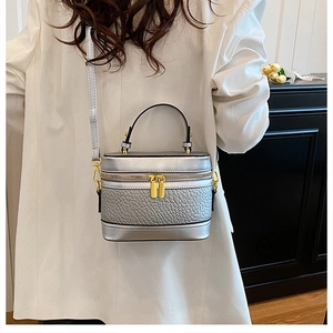 Detailed shot of silver textured leather box bag with gold hardware on white blazer