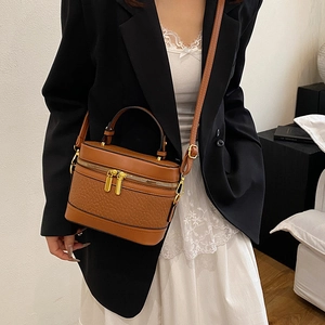 Retro brown cylinder handbag with embossed texture and gold hardware worn by a model