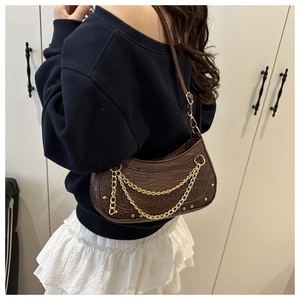 Detail of dark brown crocodile-patterned hobo bag with double gold chains and studs