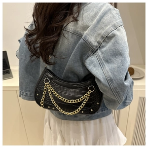 Detail of black faux crocodile skin underarm bag with decorative gold chains and rivets