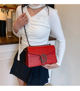 Detail of red faux snakeskin bag featuring a tiger head spur closure and metal chain strap