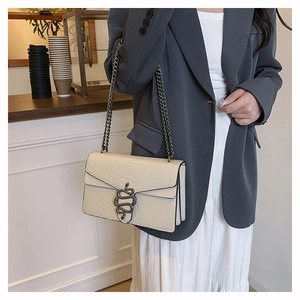 Detail of cream crocodile embossed handbag with snake clasp worn by a model in a cafe