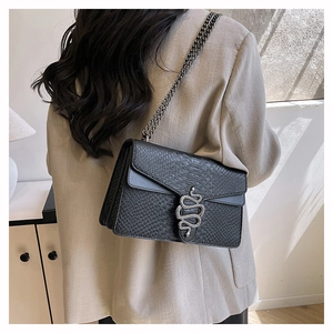 Detailed side view of a black crocodile pattern crossbody bag on a model wearing a blazer