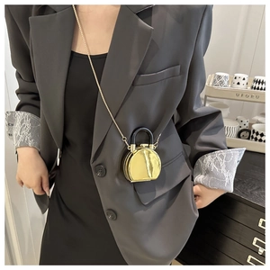 Kleine runde goldene Spiegeltasche mit Metallkette und schwarzem Griff am Model getragen