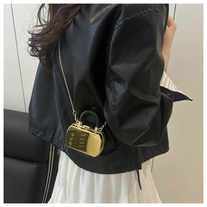 Detailansicht der goldenen Mini-Box-Tasche mit Kette über einer schwarzen Lederjacke