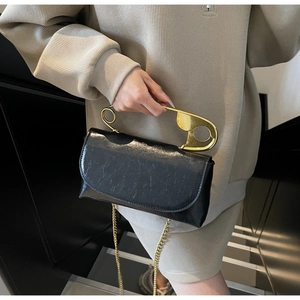 Detail of black glossy handbag with unique oversized gold safety pin handle and chain strap