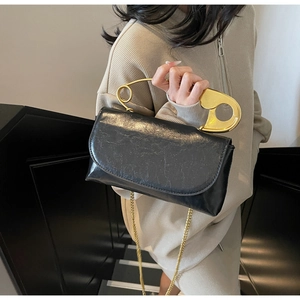 Close-up of black leather handbag with a unique large gold paperclip-shaped handle and chain