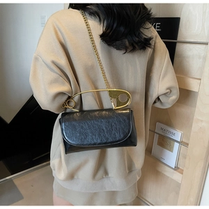 Detail of black glossy leather bag featuring oversized gold safety pin handle and chain