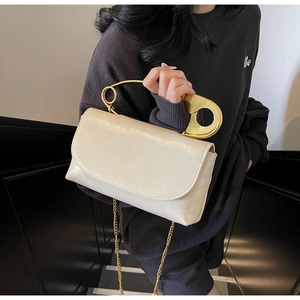 Detail view of cream PU leather crossbody bag with iconic gold safety pin handle
