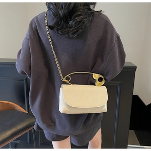 Detail view of cream leather crossbody bag with large gold safety pin handle and chain strap
