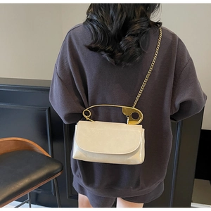 Détail du sac bandoulière en cuir beige brillant avec une poignée en épingle à nourrice