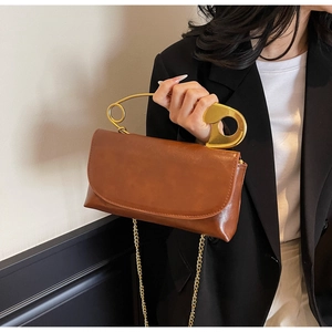 Detailed close-up of a brown leather bag featuring a unique gold safety pin handle design