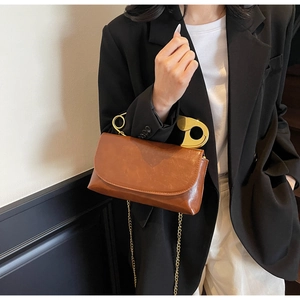 Detail view of vintage brown leather handbag featuring a creative gold safety pin top handle