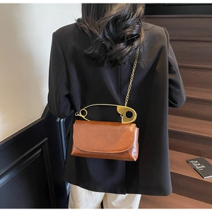 Caramel brown paperclip flap bag with gold chain strap worn by a model on stairs