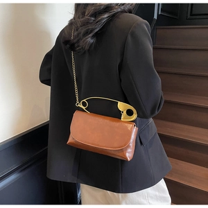 Détail d'un sac en cuir marron avec une poignée dorée en forme d'épingle de nourrice