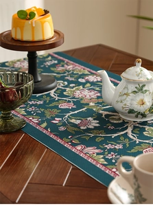 Close-up of vintage floral table runner with pink flowers on dark green fabric texture