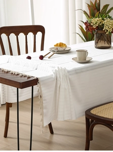 Detailed view of white hollow-out lace tablecloth with elegant beige fringe tassels