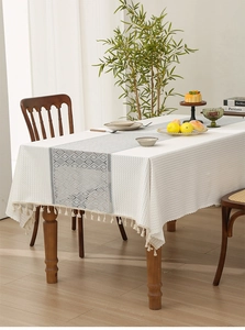 Close-up of a white jacquard tablecloth with grey patterns and beige tassel fringe edge