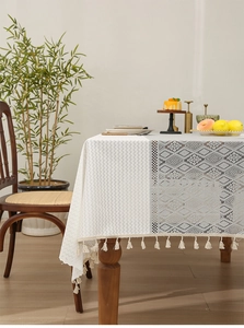 Detail of cream jacquard lace tablecloth with geometric patterns and fringe tassels