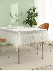 Detail of white lace tablecloth featuring delicate branch embroidery and cream fringe tassels