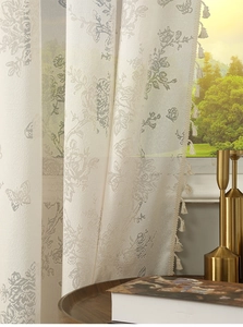 Detail of cream jacquard curtain with rose patterns, butterfly motifs and tassel fringe
