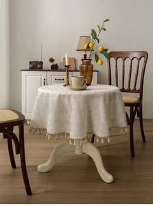 Close-up of cream linen round tablecloth featuring woven texture and tassel edges