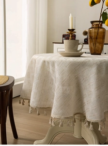 Detail of beige waffle weave texture and fringe tassels on a circular linen tablecloth