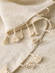 Close-up of beige linen tablecloth featuring intricate fringe tassels and woven texture