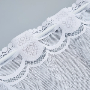 Close-up of white lace curtain featuring delicate floral embroidery and scalloped edges