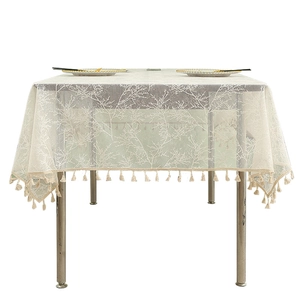 White lace tablecloth with coral embroidery and cotton fringe hanging from a wooden table