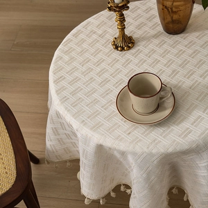 Linen round tablecloth with beige woven texture and tassel trim on a wooden dining table