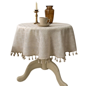 Round linen tablecloth in beige with textured weave and fringe tassels for dining tables