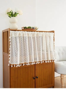 Detail of bohemian lace curtain with geometric embroidery and cotton tassels on wood cabinet