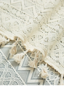 Macro detail of beige crochet lace curtain with geometric patterns and fringe tassels