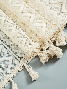 Macro detail of beige lace curtain with hollow geometric patterns and handmade tassels