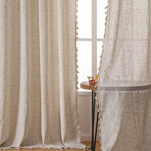 Dettaglio di tende in lino beige con bordo a nappe in un ambiente accogliente stile boho