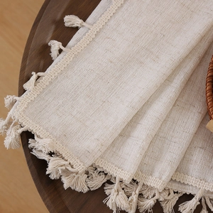 Dettaglio della trama in lino beige con nappine a frangia su una superficie in legno