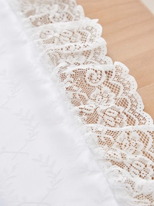 Detail van wit jacquard tafelkleed met elegante kanten rand op houten ondergrond