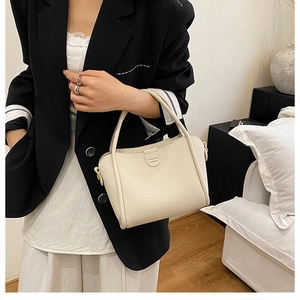 Close-up of lychee grain leather handbag with top handle held by a model in a modern room
